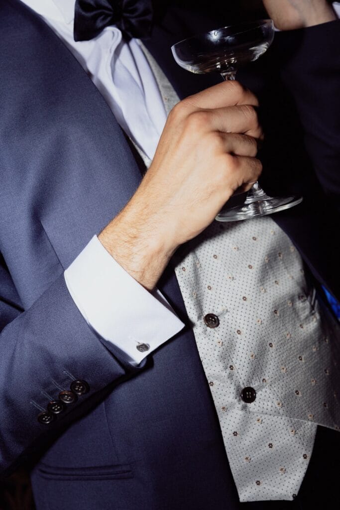 Dettaglio dello smoking blu con gilet chiaro, papillon e polsino bianco