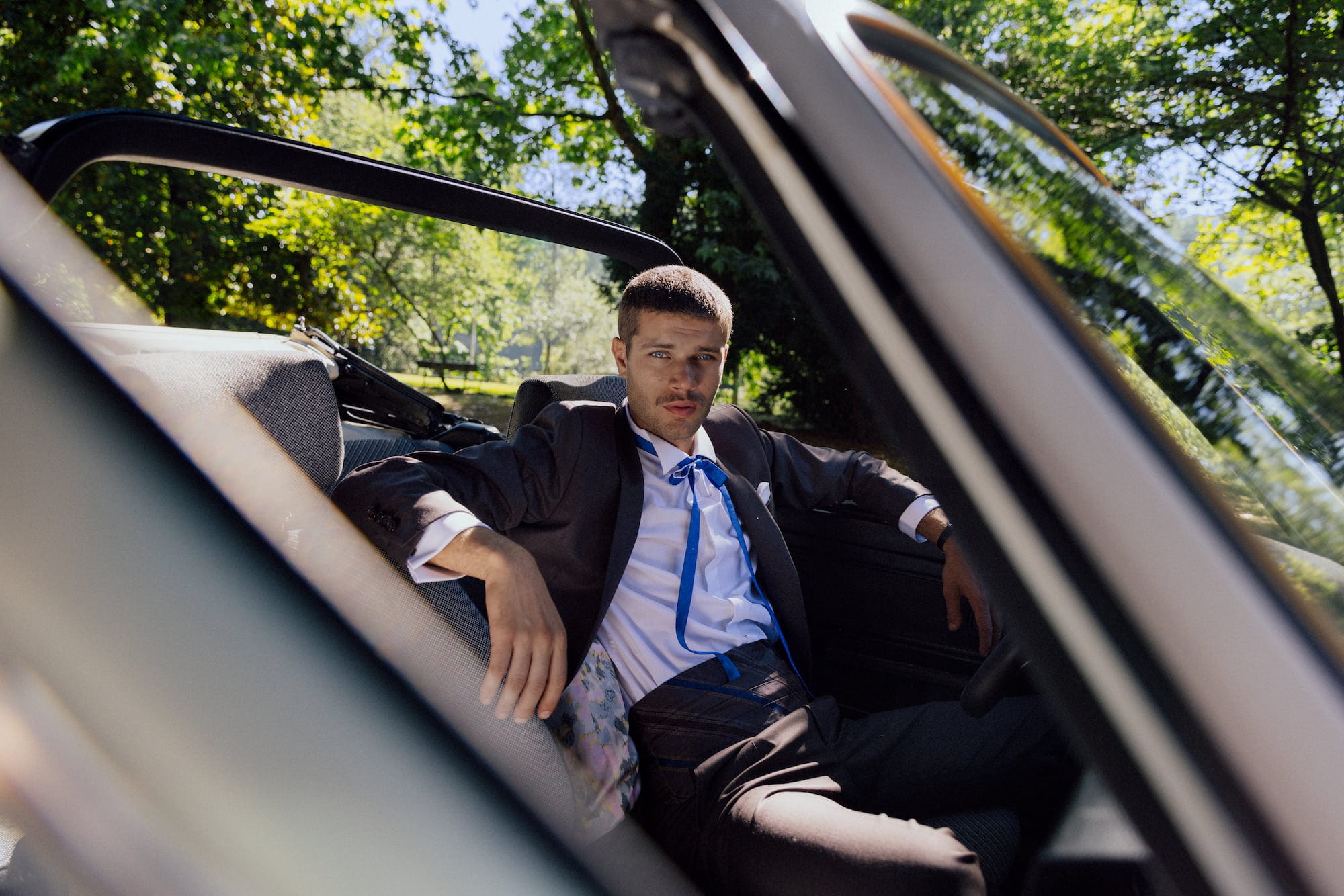 Abito sartoriale uomo scuro con cravatta blu, fotografato in una cabriolet