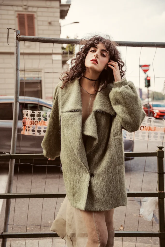 Modella con cappotto verde salvia dalla linea morbida e collo ampio, fotografata in citt&agrave;